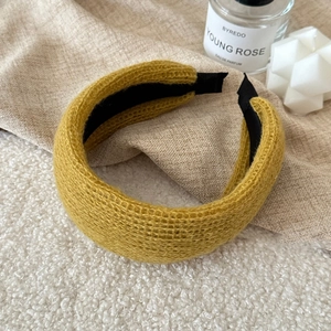 Close-up of thick knitted headband in ginger yellow with soft wool texture and black inner lining