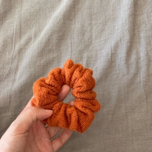 Close-up of orange knitted scrunchie showing thick wool texture and elastic band detail