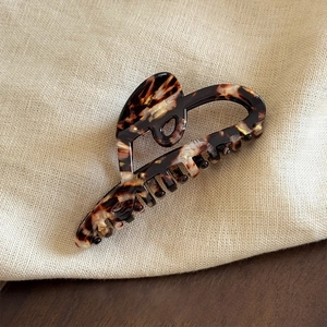 Detailed texture of tortoise shell pattern acetate heart hair claw on beige linen fabric