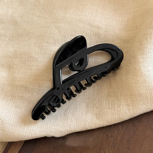 Detail of a large black acetate hair claw clip with smooth finish on a beige linen fabric