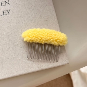 Detail of yellow plush lambswool hair comb with 11-tooth metal base on a book