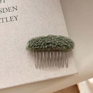 Macro shot of green faux lamb wool hair comb detail with metallic teeth on book surface