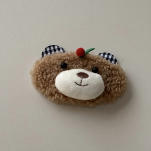 Close-up of plush brown bear hair clip featuring cherry accent and plaid ear details