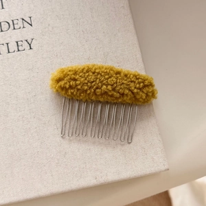 Detail view of yellow plush lamb wool hair comb with polished silver metal teeth accessory