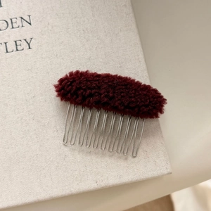 Close-up of a burgundy plush lamb wool hair comb with 10 silver metal teeth for styling