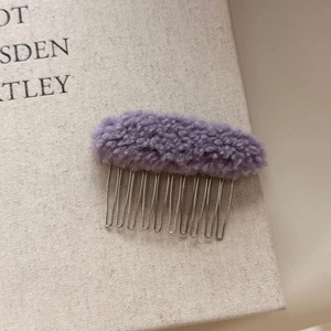 Close-up of lavender faux fur hair comb on a book showing soft texture and metal teeth