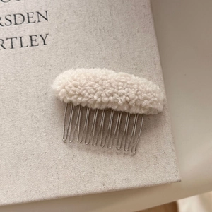 Close-up of cream lamb wool hair comb with soft fleece texture and silver metal teeth