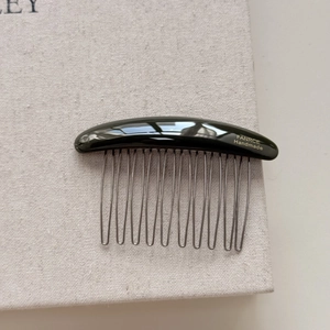 Detail of 10-tooth curved hair comb with gold handmade logo and polished black finish
