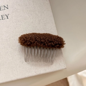 Detail of a brown fuzzy plush hair comb with ten silver metal teeth on a book background