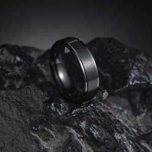 Gros plan d'une bague noire mate brossée avec bords polis sur une pierre sombre