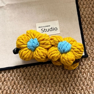 Detail of yellow hand-crocheted floral hair clip with blue centers on a canvas background