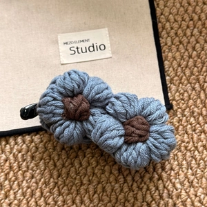 Close-up of blue knitted flowers with brown centers on a classic black banana hair clip