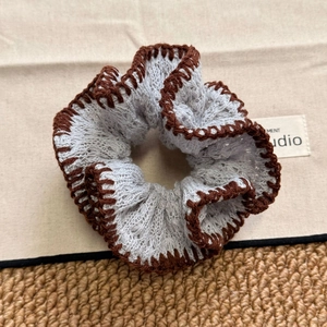 Detailed view of grey knitted scrunchie with brown stitched edge on neutral background