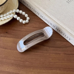 Macro detail of marbled grey acetate hair clip with gold lettering on a wooden desk
