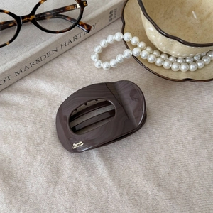 Detailed view of dark tortoiseshell hair claw clip with gold lettering on beige fabric