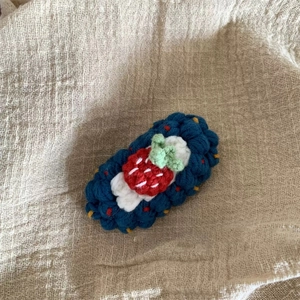 Détail d'une pince à cheveux au crochet faite main avec fraise rouge sur tricot bleu