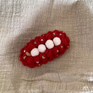 Détail d'une pince à cheveux au crochet rouge avec pompons blancs et perles de nacre