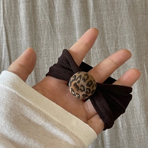 Detail of high-elastic leopard print round charm hair tie held against gray fabric