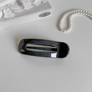 Detail of grey marble duckbill hair clip with golden script on a jewelry box