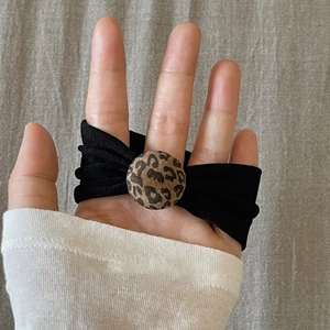 Detail of black bow hair tie with leopard print bead on elastic band shown on hand