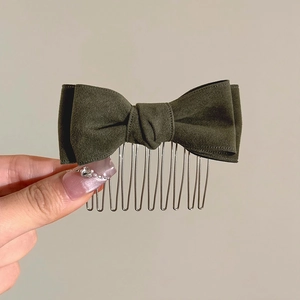 Close-up of a dark green plush bow hair comb held by hand with fine metal teeth