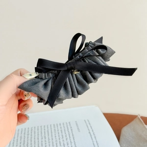 Detail of grey pleated fabric hair claw clip with black silk ribbons and gold heart charm