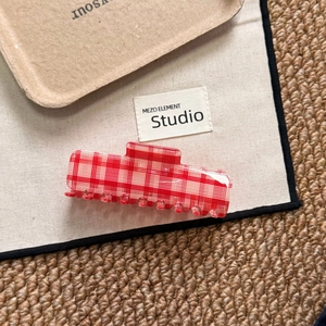 Macro detail of red and white checkered acetate hair claw clip on a minimalist wooden tray