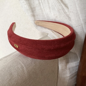 Detail of burgundy faux suede headband featuring a gold-toned handmade metal tag