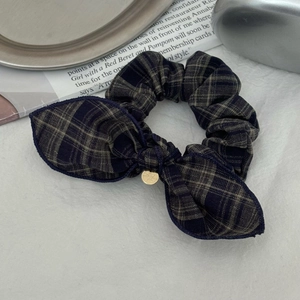 Détail d'un chouchou vintage à carreaux avec nœud et pendentif doré sur tissu plissé