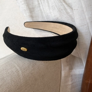 Detail of wide black suede headband with a gold metal plate showing Hand made text