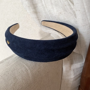 Close-up of a wide navy blue faux suede headband featuring an elegant gold metal button