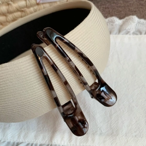 Detailed view of tortoiseshell pattern duckbill hair clips on a vintage fabric background