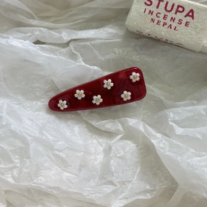 Dettaglio di un fermaglio per capelli in acetato rosso con trama marmorea e fiori bianchi