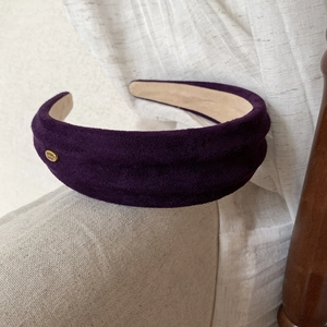 Detail view of the deep purple suede headband featuring a gold Hand Made metal tag