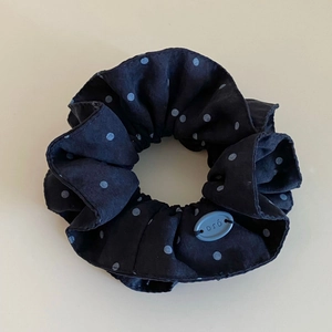 Detail of black polka dot hair scrunchie featuring a soft pleated fabric and blue logo tag