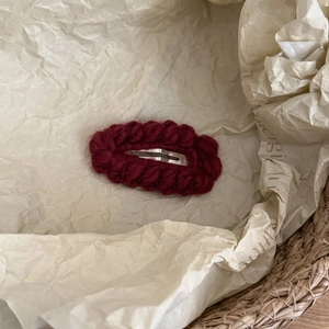 Close-up of deep red handmade crochet hair clip with metal spring fastener on rustic basket