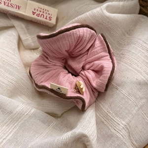 Detail eines rosa Scrunchie mit braunem Rand und handgemachtem Etikett auf Stoff