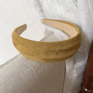 Detailed macro shot of a mustard yellow faux suede padded headband on a sofa