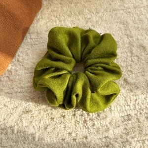Close-up of olive green knitted scrunchie fabric texture on soft cream background
