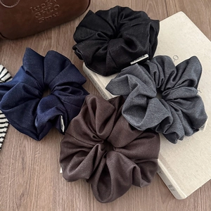 Set of four Korean-style fabric scrunchies in neutral colors on a minimalist wood background
