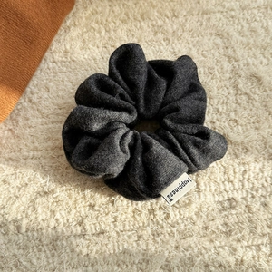 Detail of dark grey knit scrunchie with Happiness woven label on soft plush surface