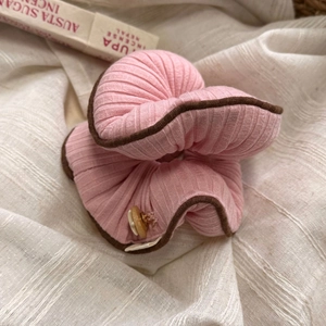 Rosa Rippstrick-Haargummi mit braunem Saum und Holzknopf auf beigem Stoffhintergrund