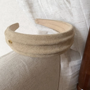 Detail of khaki faux suede wide headband with a golden oval metal emblem attachment