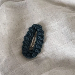 Macro detail of dark teal crochet knit texture and silver metal snap hair clip on linen