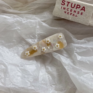 Dettaglio del fermaglio per capelli in acetato con fiori bianchi e trama marmorizzata
