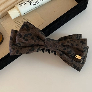 Detail of leopard print bow hair clip with golden metal tag on a lifestyle background