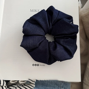 Detail of navy blue denim fabric scrunchie with pleated texture on a white book