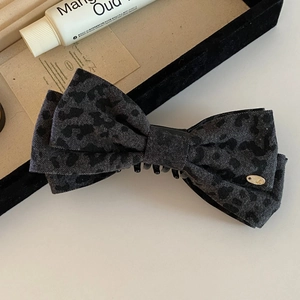Detail of grey leopard print fabric bow clip with gold logo on a minimalist background