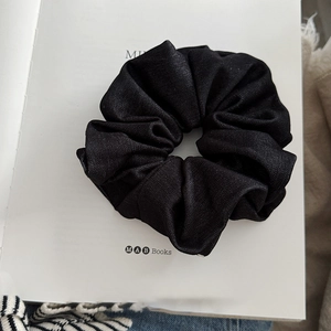 Macro view of oversized black scrunchie with pleated fabric texture on a book