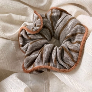 Detailed view of striped knit scrunchie with brown faux fur trim on white linen fabric